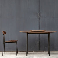 Modern wooden dining table and chair in rich brown tones with black metal legs against a gray background.