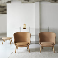 Set of two tan modern chairs with smooth contours, complemented by a light-colored rug and sleek glass table.