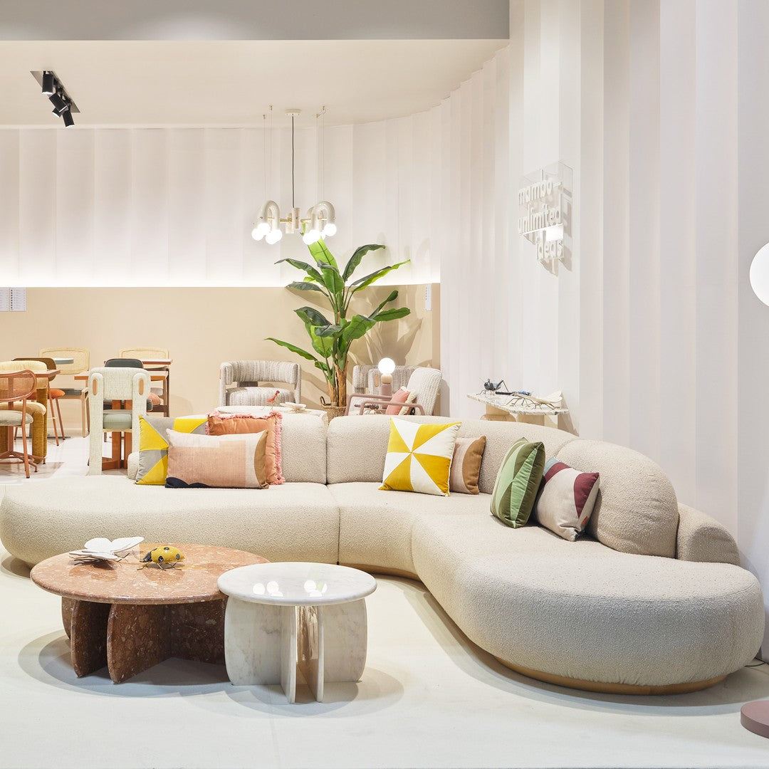 Modern beige curved sofa adorned with colorful cushions in yellow, green, and pink geometric patterns. Elegant decor elements.