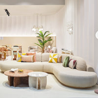 Modern beige curved sofa adorned with colorful cushions in yellow, green, and pink geometric patterns. Elegant decor elements.