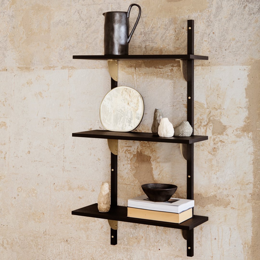 Black wooden shelves against a textured beige wall, showcasing a mix of dark and light decor items.