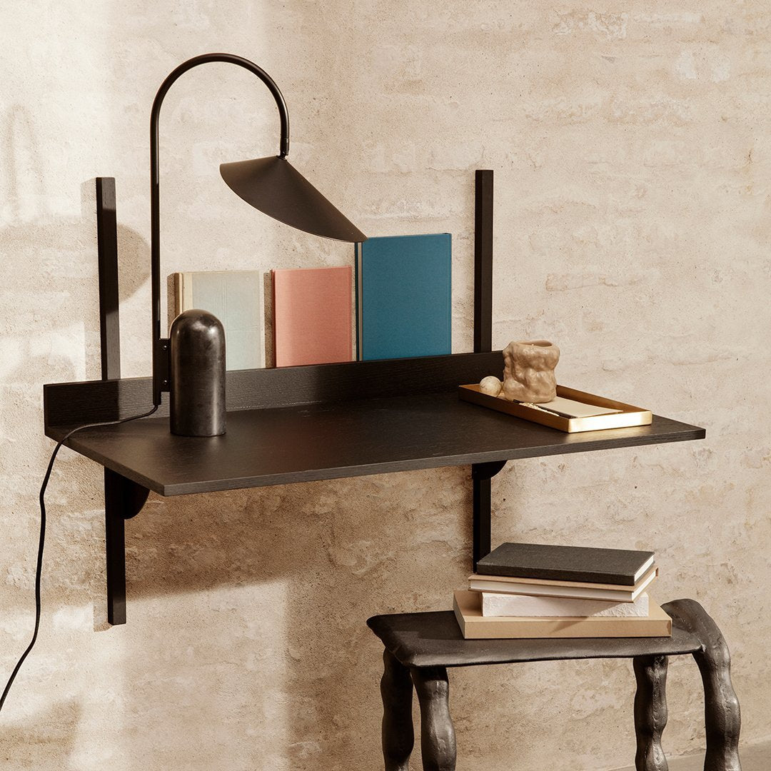 Minimalist black wall-mounted desk with geometric patterns, accented by pastel book colors and a sleek lamp.