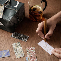 "Colorful patterned gift tags in blues, greens, and neutrals, with a sleek black packaging and wood background."