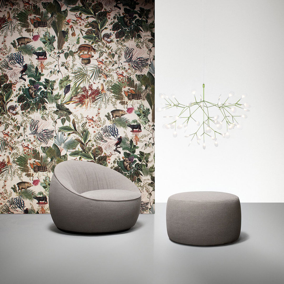 "Round gray armchair and ottoman against vibrant floral wallpaper with green, red, and blue patterns."