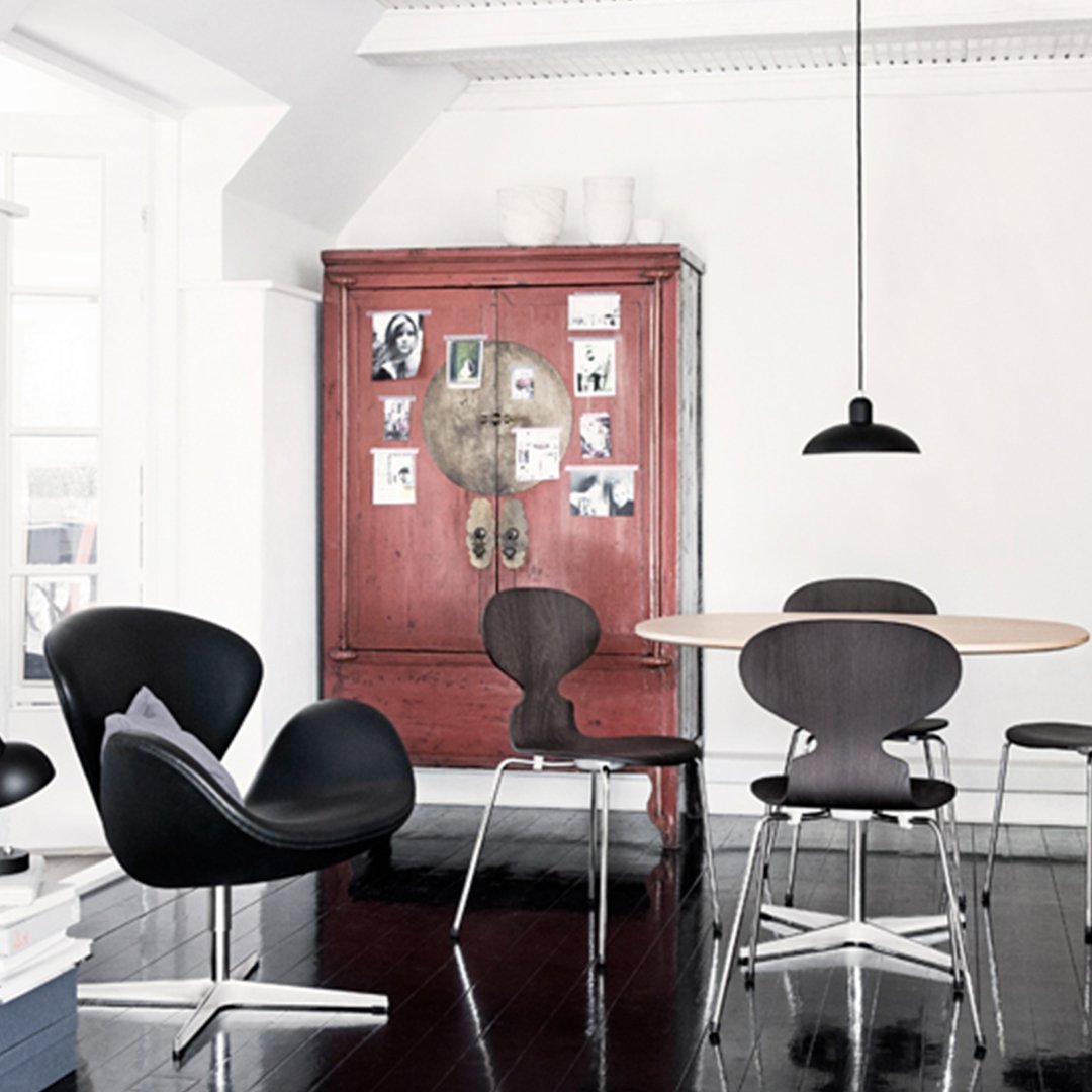 Modern black chairs contrast with a vintage red cabinet in a minimalist dining room setting. Sleek lines and smooth surfaces.