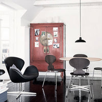 Modern black chairs contrast with a vintage red cabinet in a minimalist dining room setting. Sleek lines and smooth surfaces.