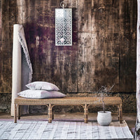 Woven bamboo bench with neutral-colored cushions, set against a rustic wooden wall and patterned light fixture.
