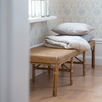 Rattan bench with neutral cushions against pale blue floral wallpaper in a light, airy room.