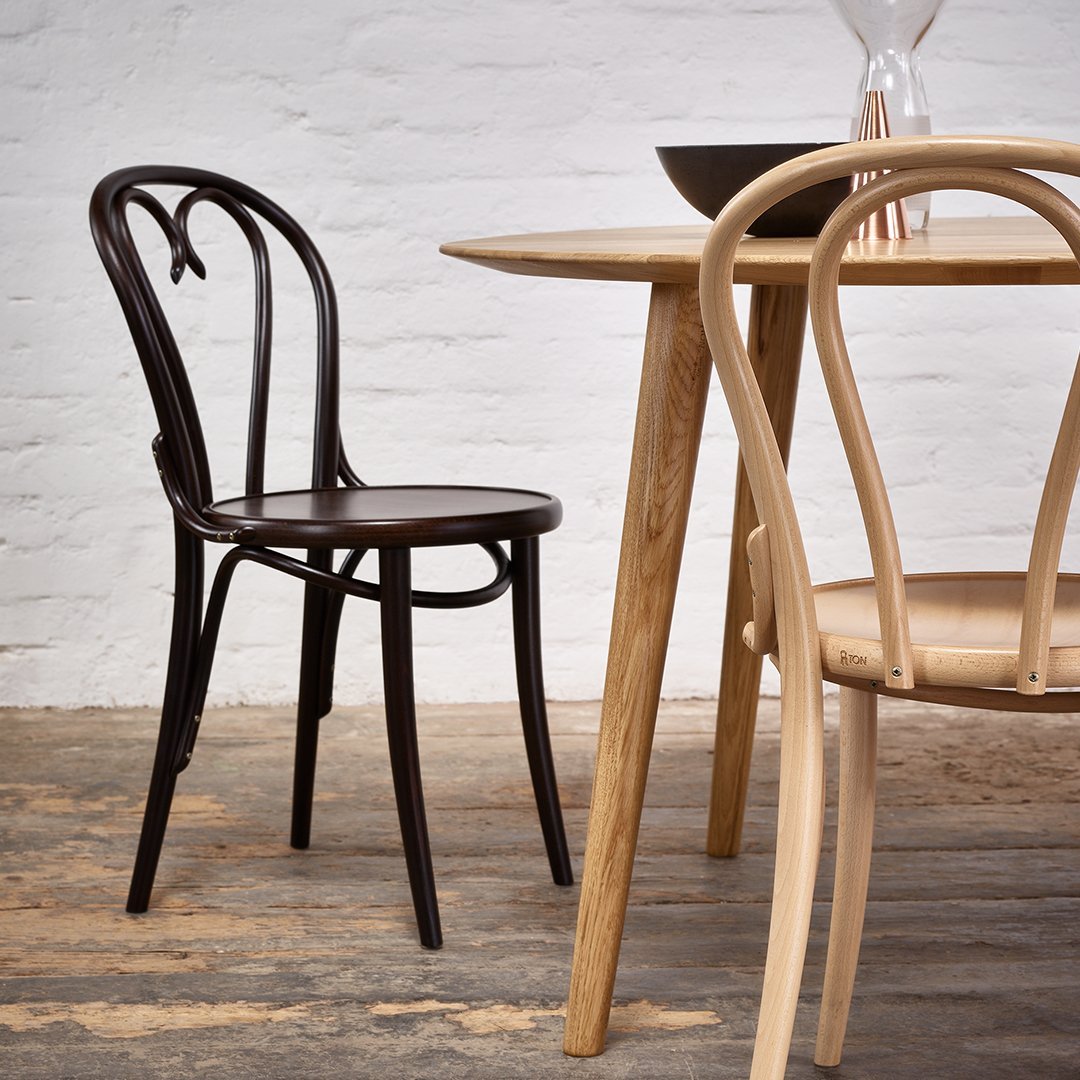 Dark brown bentwood chair beside a light wood table on a rustic floor, showcasing classic design and natural tones.