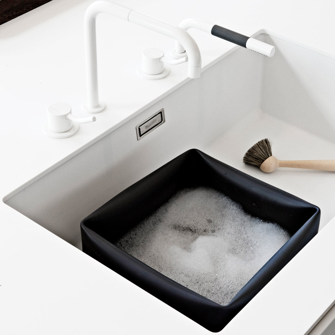 Black square sink basin with white bubbles, against a minimalist white countertop and faucet.
