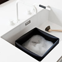 Black square sink basin with white bubbles, against a minimalist white countertop and faucet.