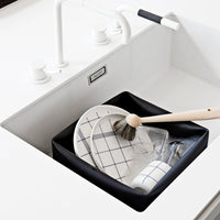Black dish rack with white dishes featuring grid patterns and a wooden brush in a modern sink setting.