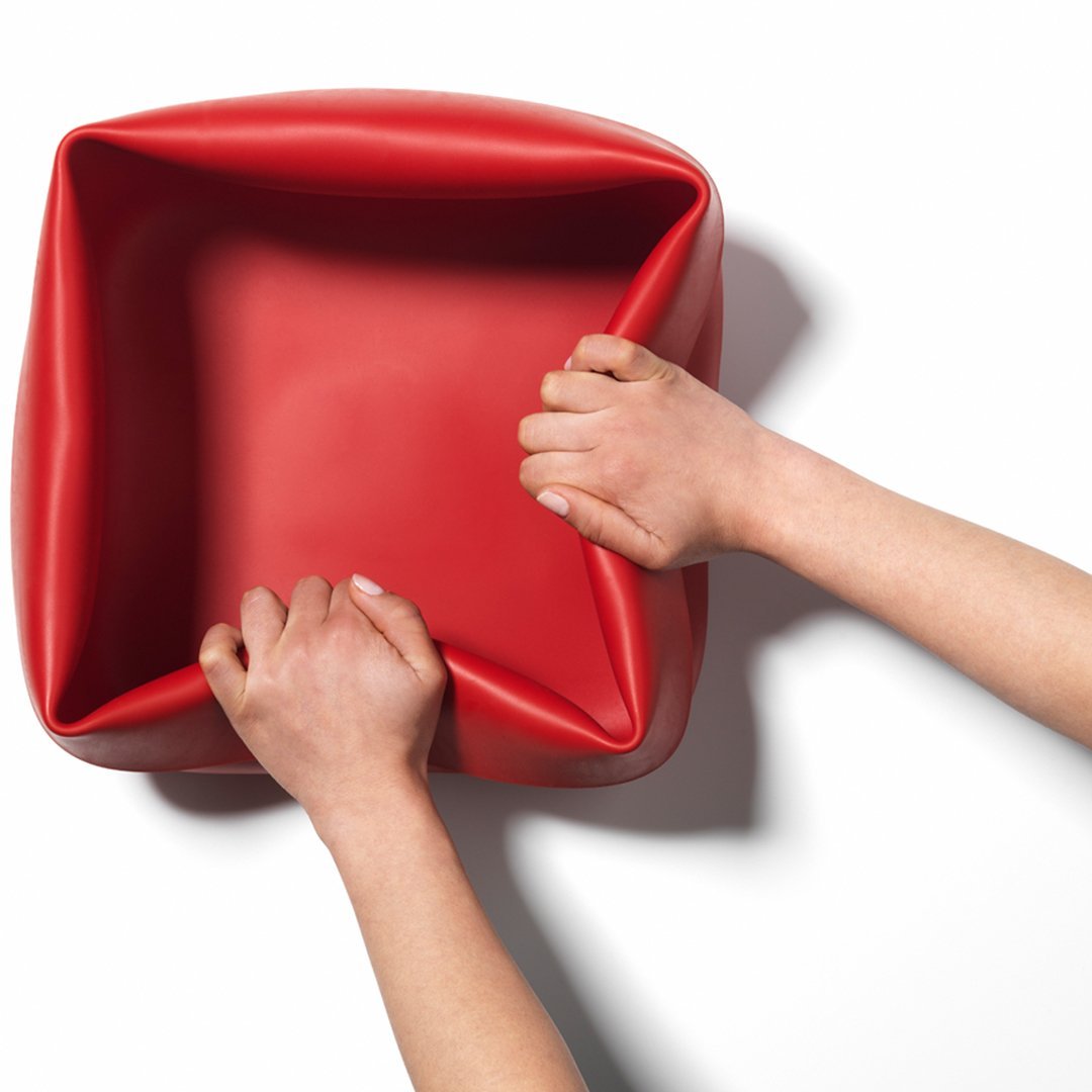 Bright red square container with smooth, glossy finish, held by two hands against a white background.
