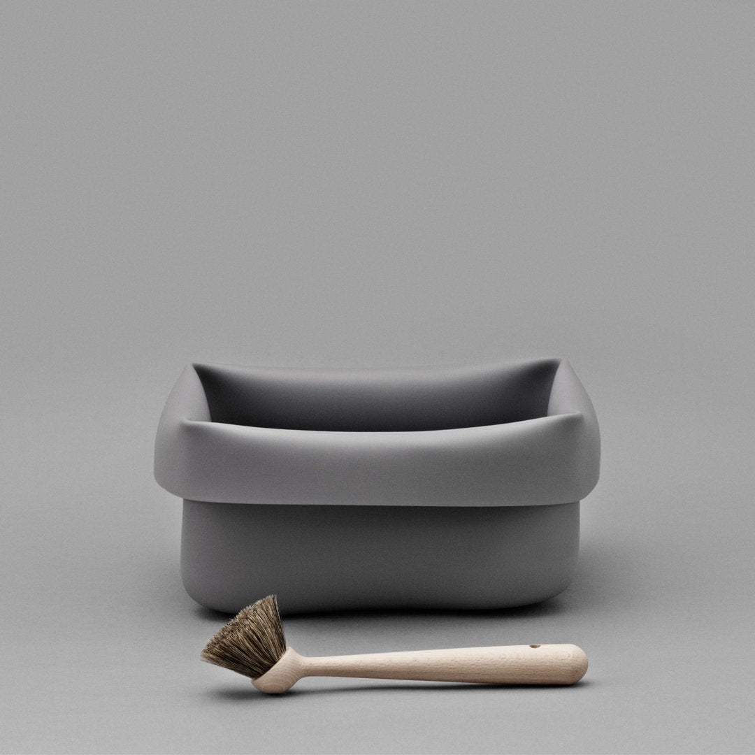 Gray rectangular storage container with a smooth finish, paired with a soft-bristled brush in pale beige.