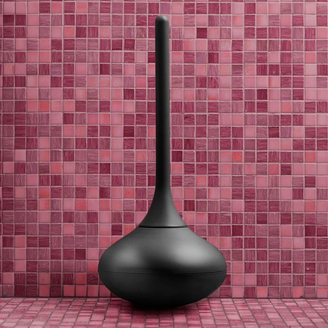 Black minimalist vase against a vibrant pink mosaic tile background, highlighting smooth curves and bold contrast.