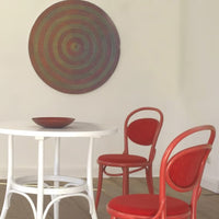Red circular pattern wall art with red upholstered chairs and a white round table. Modern, vibrant decor for any space.