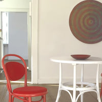 Red chair and bowl against a neutral backdrop, featuring a patterned round wall art in earthy tones.