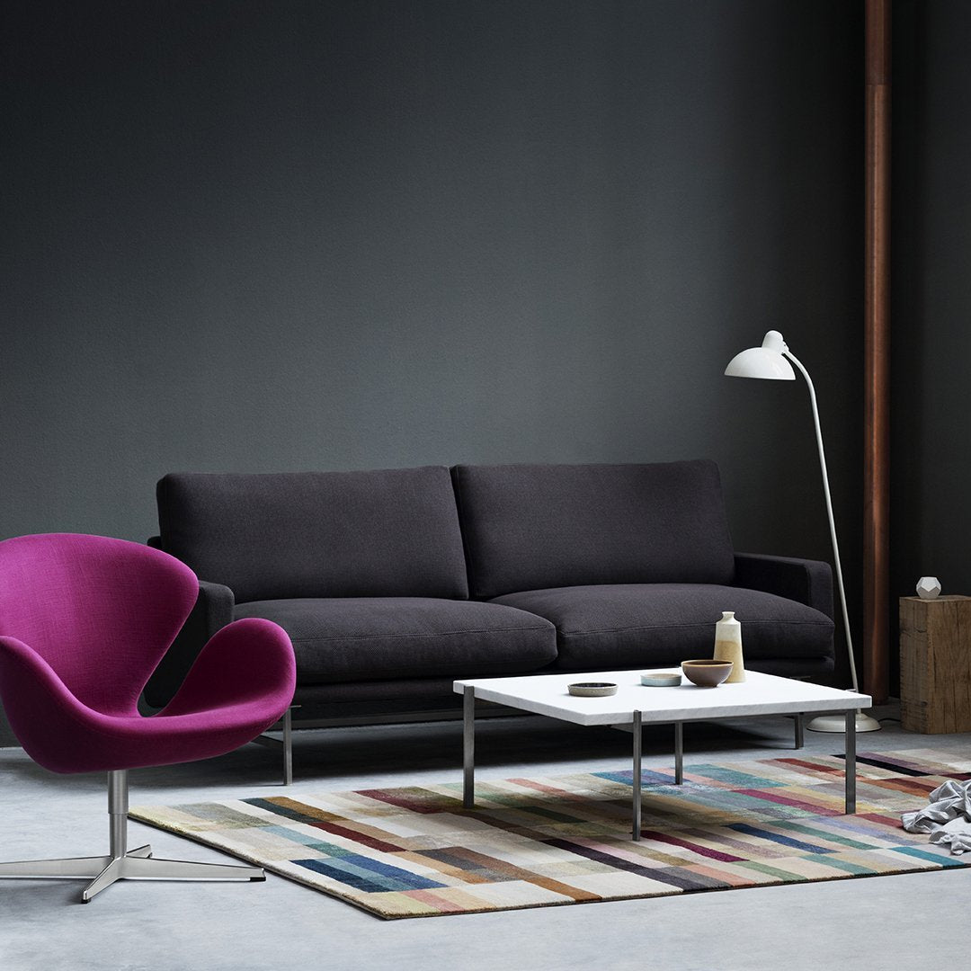 Modern black sofa with vibrant purple chair and colorful striped rug against a dark wall backdrop.
