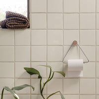 Soft beige tiled wall with a textured pattern, featuring a black and brown woven towel and greenery accent.