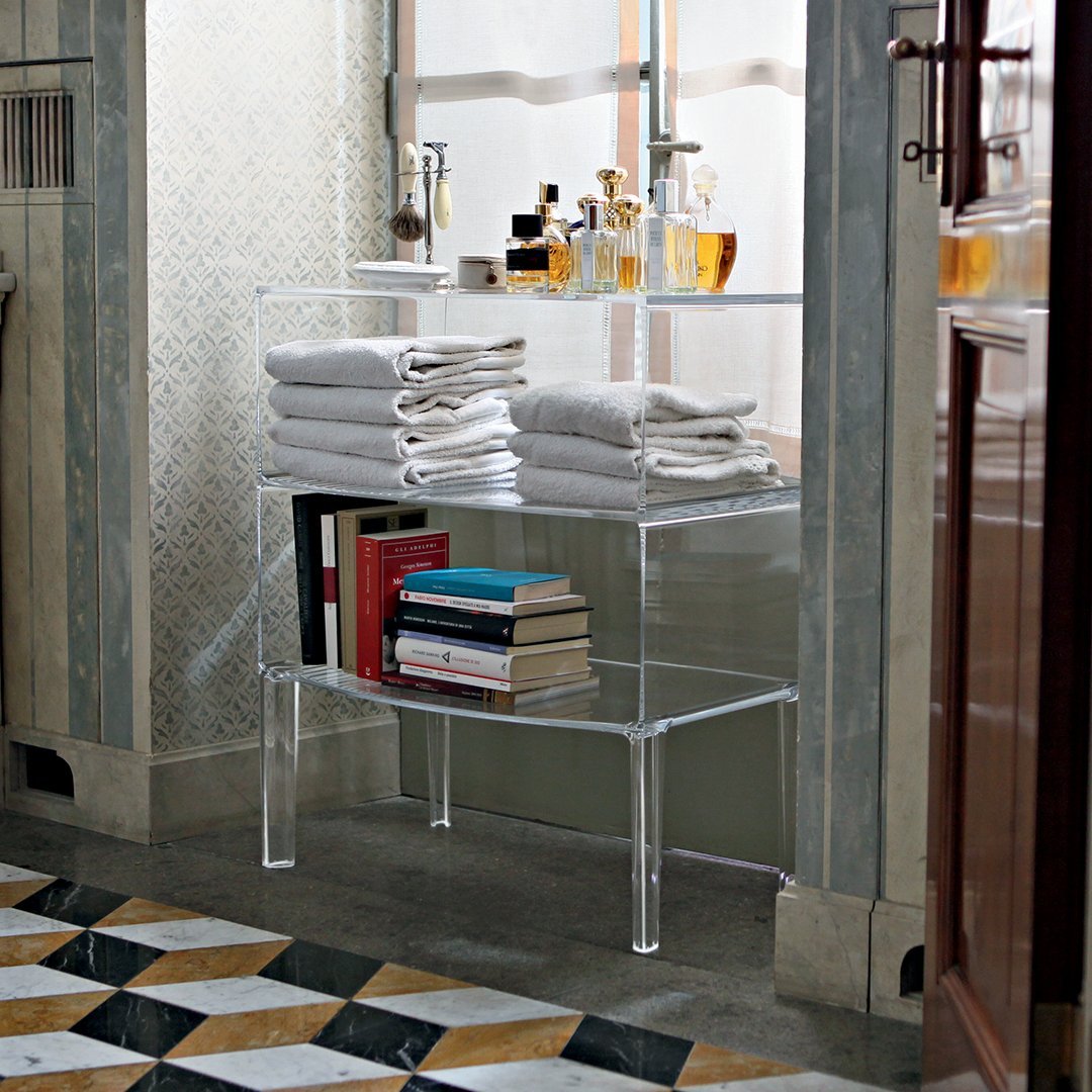 Clear acrylic shelving unit with stacked white towels and colorful books on a patterned tiled floor.