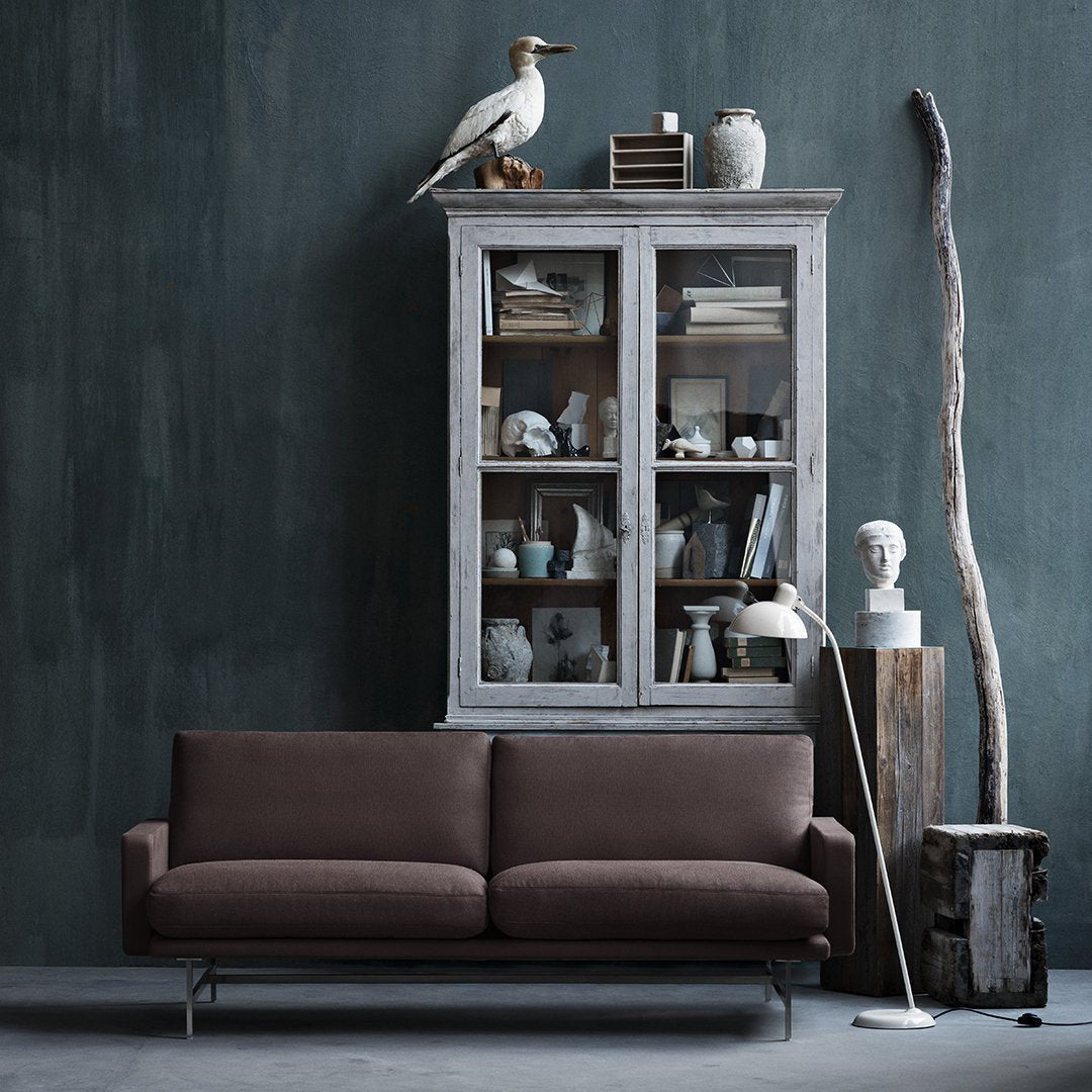 Brown sofa with a sleek design against a textured dark green wall, featuring neutral ceramics and natural wood accents.