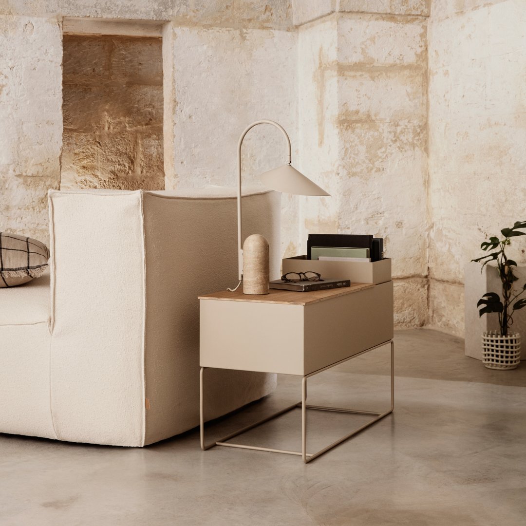 Beige sofa with minimalistic design, light wood nightstand, and neutral tones in a modern, textured setting.