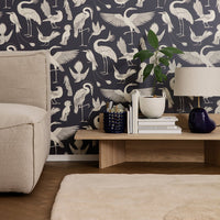 "Dark blue wallpaper with white crane and bird patterns, complemented by neutral furniture and decor."