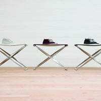 "Three pairs of sneakers in white, burgundy, and black displayed on sleek silver stools against a light background."