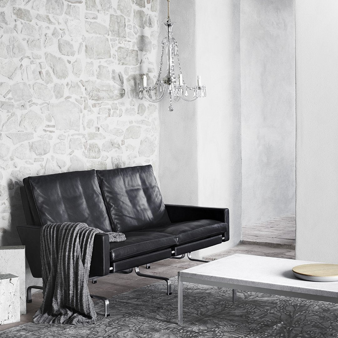 Black leather sofa with sleek lines, complemented by a textured gray throw and a light gray geometric rug.