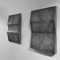 Two textured wall art pieces in shades of gray with unique geometric designs. Ideal for modern decor.
