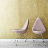 "Two modern chairs in soft pink fabric against a textured yellow wall, showcasing a minimalistic design."