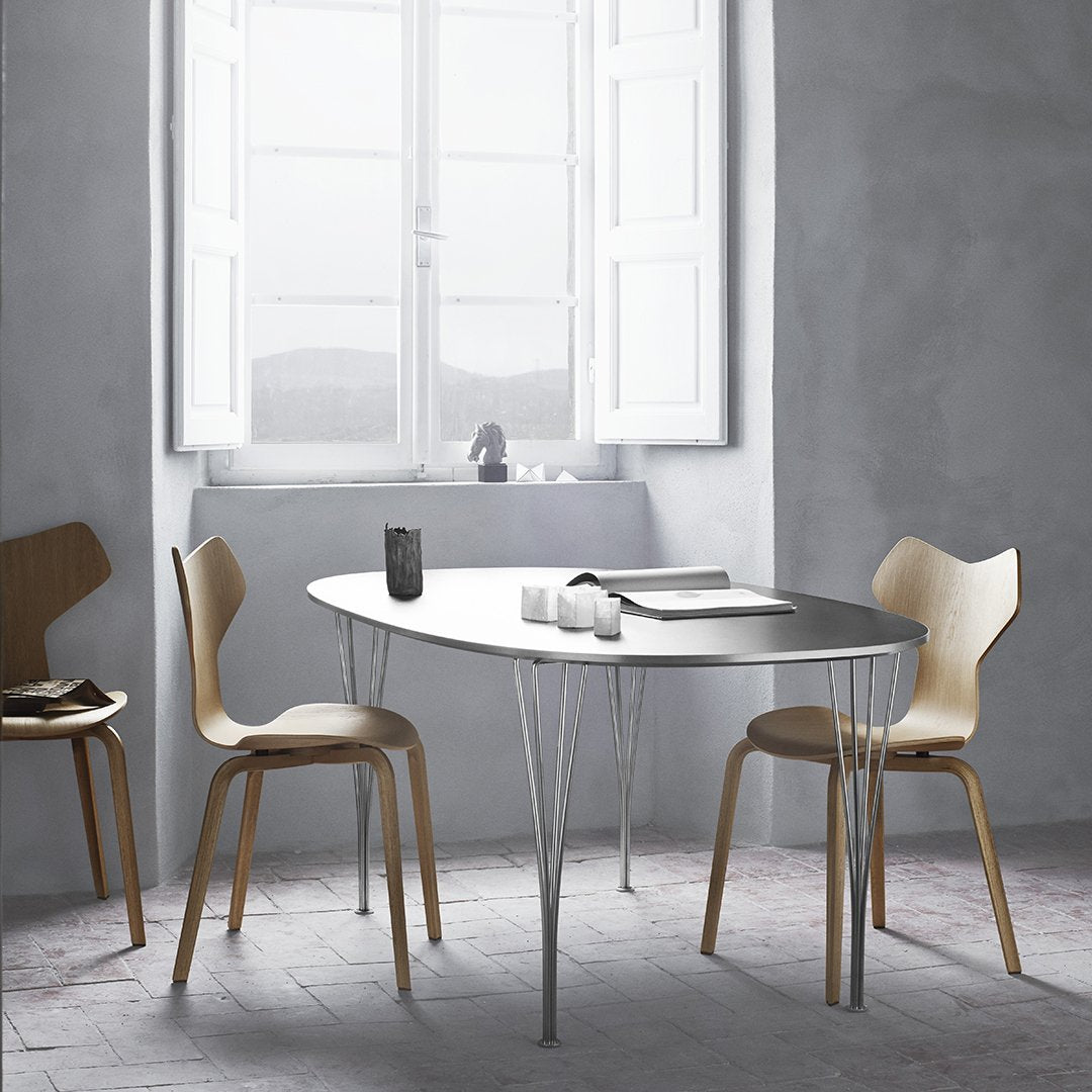 Modern oval dining table with a sleek gray surface and natural wood chairs in a minimalist, neutral-toned setting.