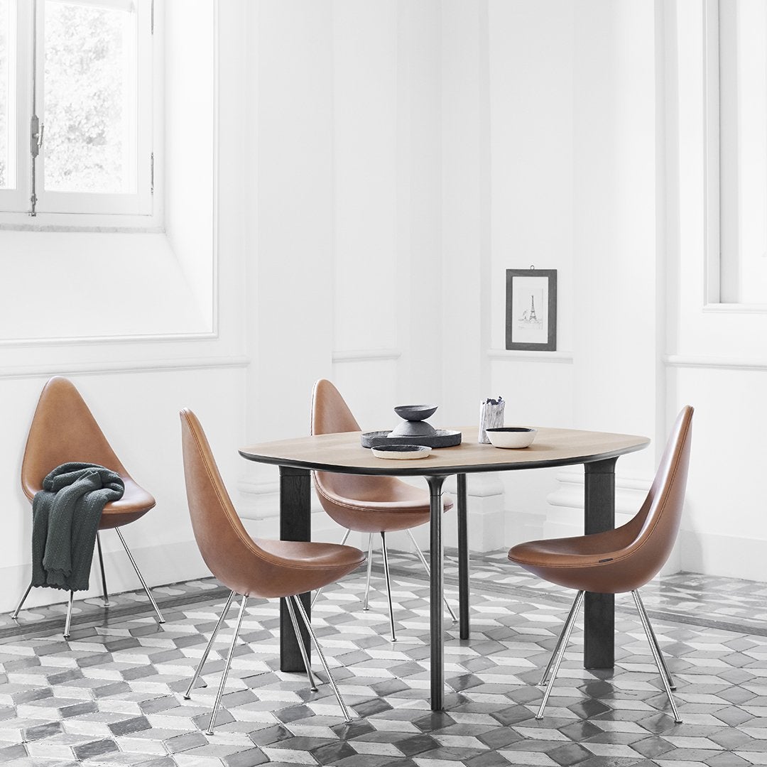 Brown curved chairs around a round wooden table on a black and white patterned tiled floor in a bright, minimalist room.