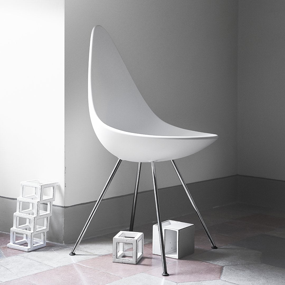 White modern chair with smooth curves and sleek metallic legs, set against a minimalist gray and pastel background.