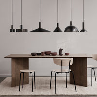 Modern dining table with a wooden finish, black pendant lights, and earthy-toned ceramic bowls on a neutral rug.