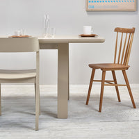 Beige dining table with a smooth finish, paired with a light beige chair and a natural wood slatted chair.