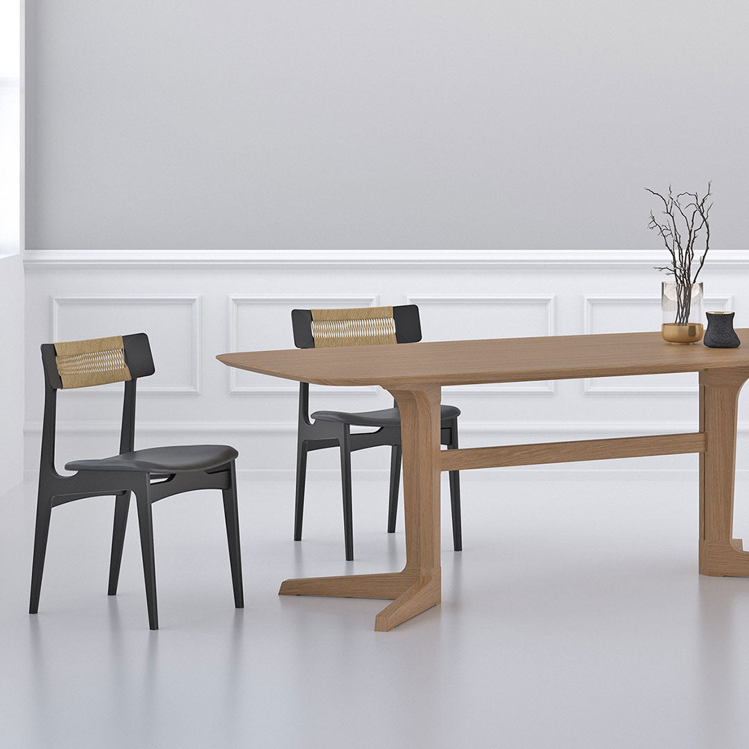 Natural wood dining table with beige finish and black chairs featuring woven backs, set in a minimalistic white room.