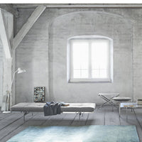 Minimalist interior featuring a soft blue rug, gray walls, and light wood accents, creating a serene atmosphere.