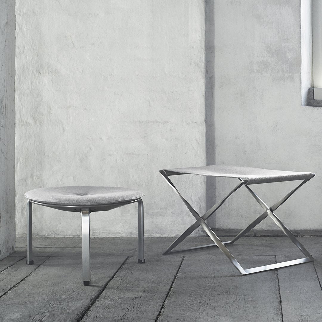 Two modern tables with a sleek silver finish and minimalist designs, set against a textured gray wall.