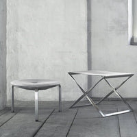 Two modern tables with a sleek silver finish and minimalist designs, set against a textured gray wall.