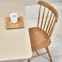 Neutral beige table with a warm wooden chair and a white mug on a light wooden surface. 