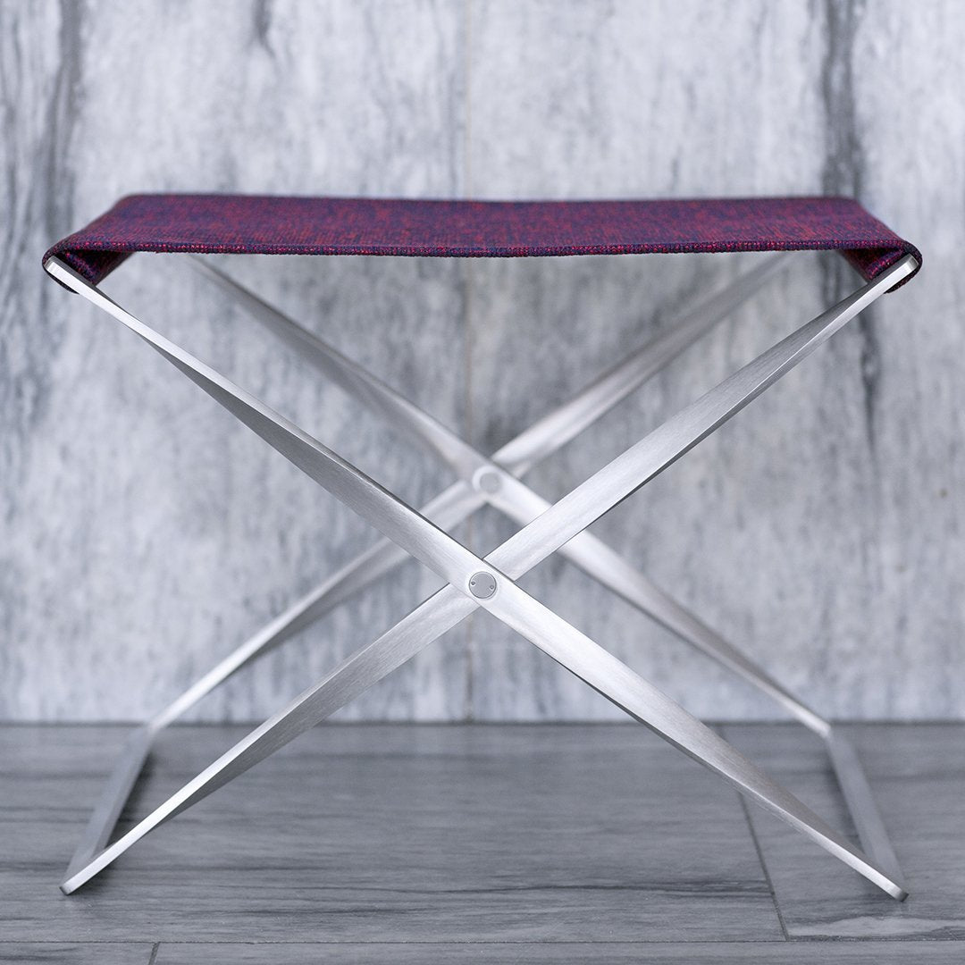 Purple patterned fabric seat on a sleek silver folding chair against a gray backdrop. Modern and stylish design.