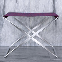 Purple patterned fabric seat on a sleek silver folding chair against a gray backdrop. Modern and stylish design.