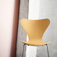 "Stylish yellow butterfly chair with a smooth finish against a textured gray wall and soft pink background."