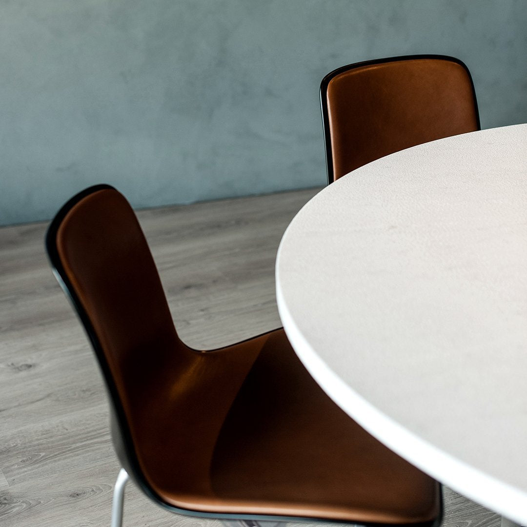 White round table with brown leather chairs against a muted blue wall, featuring light wood flooring.