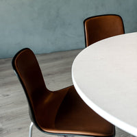White round table with brown leather chairs against a muted blue wall, featuring light wood flooring.