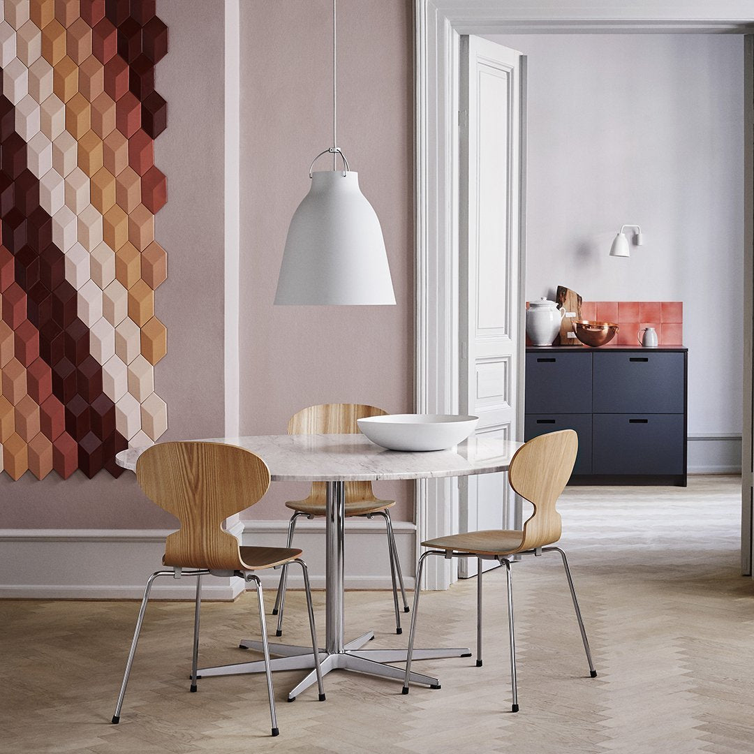 Hexagonal wall pattern in warm hues of red, brown, and peach, with a minimalist white table and light wood chairs.