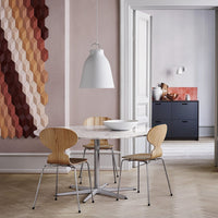 Hexagonal wall pattern in warm hues of red, brown, and peach, with a minimalist white table and light wood chairs.