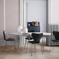Elegant round white table with sleek black chairs, set against soft pink walls and minimalist decor.