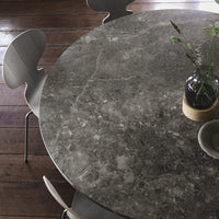 Elegant round gray marble table with subtle veining patterns, complemented by minimalist wooden chairs.